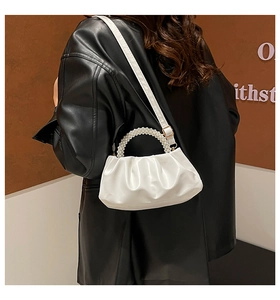 Detail of white pleated cloud bag with pearl handle worn over a black jacket