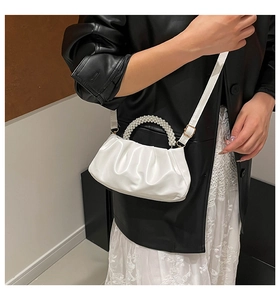 Detail of white pleated handbag featuring a pearl bead handle and adjustable strap