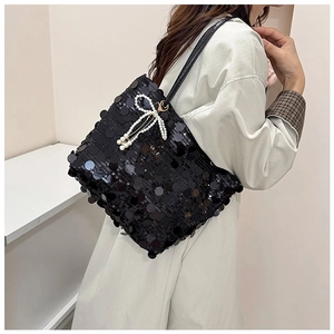 Detail of black sequin bucket bag featuring a white pearl bow and gold metal chain strap
