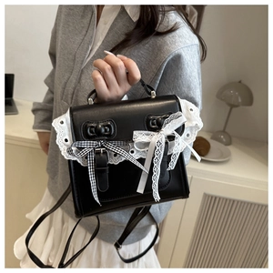 Détail du sac en cuir noir avec bordure en dentelle blanche et nœud à carreaux