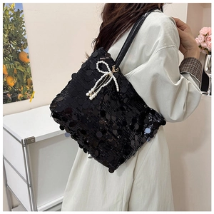 Detail of black sequined tote bag featuring a white pearl bow tassel charm on the strap