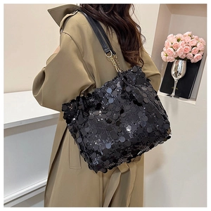 Détail du sac à bandoulière à paillettes noires avec chaîne dorée sur un trench-coat
