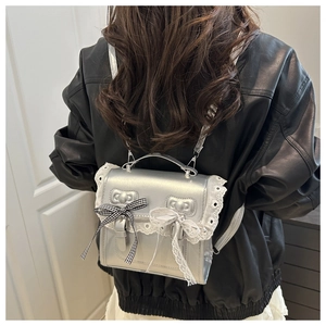 Detail eines silbernen Mini-Rucksacks mit Spitzenbesatz und Schleife auf Lederjacke