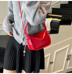 Detail view of red glossy patent leather crescent bag with leather chain strap and top handle