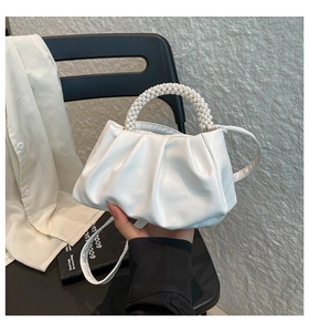 Close-up of white pleated cloud bag featuring an elegant multi-layer pearl top handle