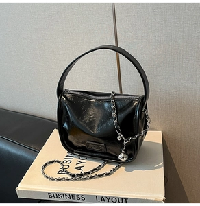 Gros plan sur le sac en cuir verni noir avec chaîne argentée et pendentif sphérique