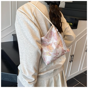 Detalle de bolso saco de satén rosa con jacquard de mariposas y borla larga plateada