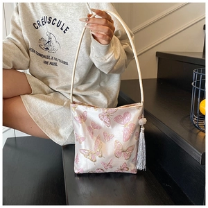 Detalle del bordado de mariposa rosa y borlas grises en un bolso tipo cubo de satén