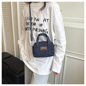 Detailed shot of dark blue denim crossbody bag featuring brown leather patch detail
