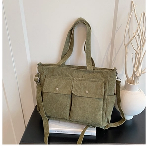Detail view of dark green corduroy tote bag featuring two front pockets and adjustable strap