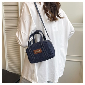Detail of blue denim crossbody bag featuring brown leather patch and white contrast stitching