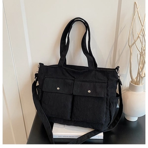 Close-up of black corduroy tote bag showing front utility pockets and textured fabric