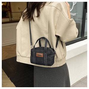 Detail of vintage black denim bag with white contrast stitching and brown leather patch