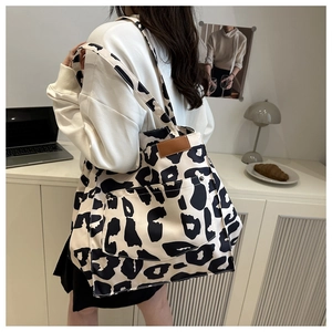 Close-up of black and white spotted tote bag with front pocket and leather patch detail