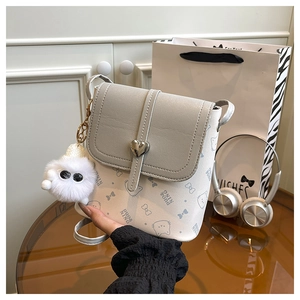 Detail of grey cat-patterned crossbody bag with heart clasp and plush pompom charm