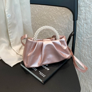 Pink satin pleated cloud bag with pearl handle and crossbody strap on black books