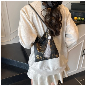 Detalle de un bolso cubo negro con patrón de mariposa dorada y borla plateada