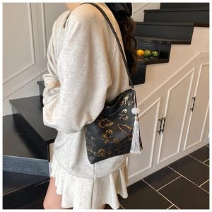 Detalle del bolso negro de hombro con estampado de mariposa dorada y borla blanca