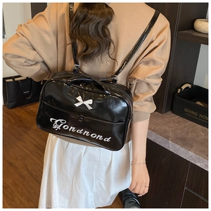 Detailed back view of black patent leather backpack with white bow and letter embroidery