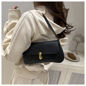 Detail of black pebbled leather baguette bag with gold metal clasp on model's shoulder