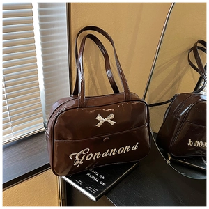 Macro view of dark coffee patent leather tote bag with cream bow and fine embroidery
