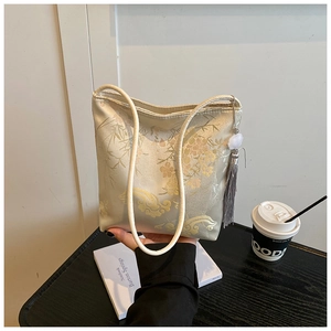 Detalle del bordado de flores rosas y nubes doradas en bolso tipo cubo de seda con borla