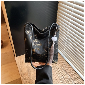Detalle de bolso cubo negro estilo chino con bordado de mariposa dorada y borlas de seda