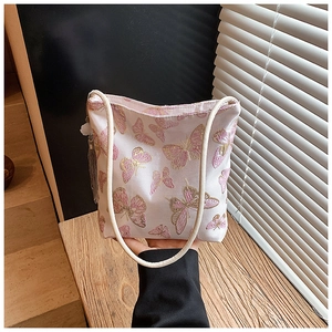 Detalle de bordado de mariposa rosa y borla gris en un bolso tipo cubo