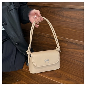 Detail of beige underarm bag with silver bow ornament and knotted rope strap on wood stairs