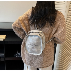 Silver metallic backpack with 'Toick OR Traet' print shown on a model in a cozy setting