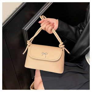 Detail of beige flap bag featuring silver bow buckle and tubular tied handle