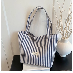 Detail of blue and white striped canvas tote bag with square fabric patch on dark surface