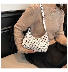 Detail of white corduroy hobo bag featuring black bow embroidery on model's shoulder