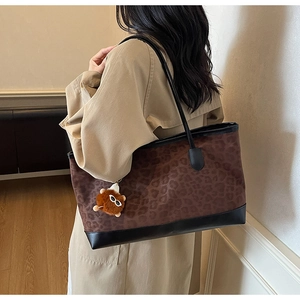 Detail of leopard print tote bag with brown plush bear charm worn by a model