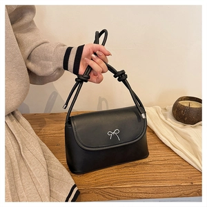 Detail of matte black crossbody bag featuring a silver metal bow and knotted handle