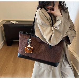 Detail of leopard print tote bag with black leather trim and plush charm accessory