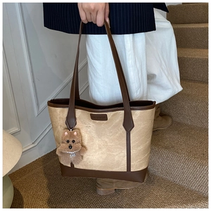 Detail of a large canvas tote bag with brown leather handles and a plush bear charm