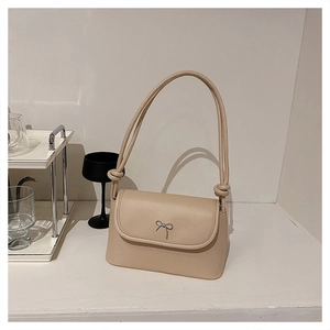 Detail of beige crossbody bag featuring a metal bow clasp and knotted shoulder strap
