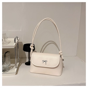 Detail of beige shoulder bag featuring silver bow logo and knotted strap accents