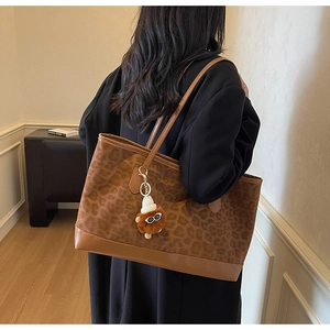 Detail of a large leopard print tote bag with brown leather trim and plush charm
