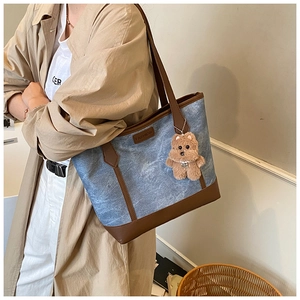 Detail of blue denim tote bag with brown leather trim and cute bear charm accessory