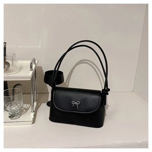 Detail of black crossbody bag with silver metal bow and premium textured synthetic leather