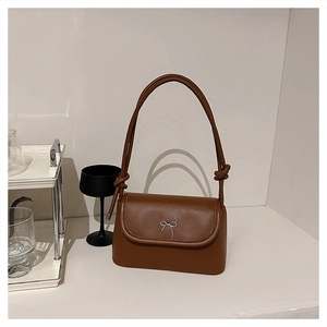 Detail of a brown leather shoulder bag with a silver bow and knotted strap design