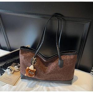 Detail of leopard print tote bag with black leather base and plush bear charm on desk