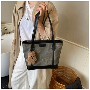 Detail of grey canvas tote bag with black leather trim and cute brown plush bear charm
