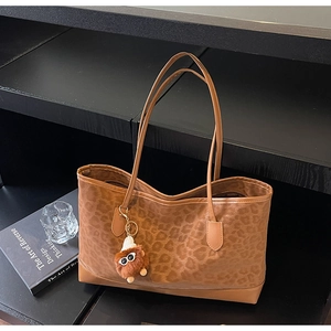 Macro shot of brown leopard print tote with a plush monster charm and leather corner detail