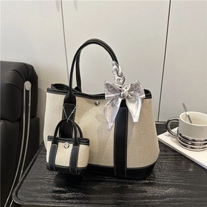 Canvas and black leather tote bag with silk scarf and mini charm on a wooden table
