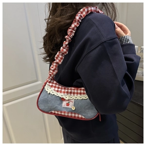 Detail of denim shoulder bag featuring lace edges, red plaid pattern and ruffled strap