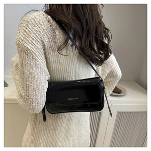 Close-up of black glossy patent leather shoulder bag with gold logo on a white dress