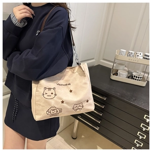 Detail of beige nylon tote bag featuring cartoon cat prints and silver chain shoulder strap